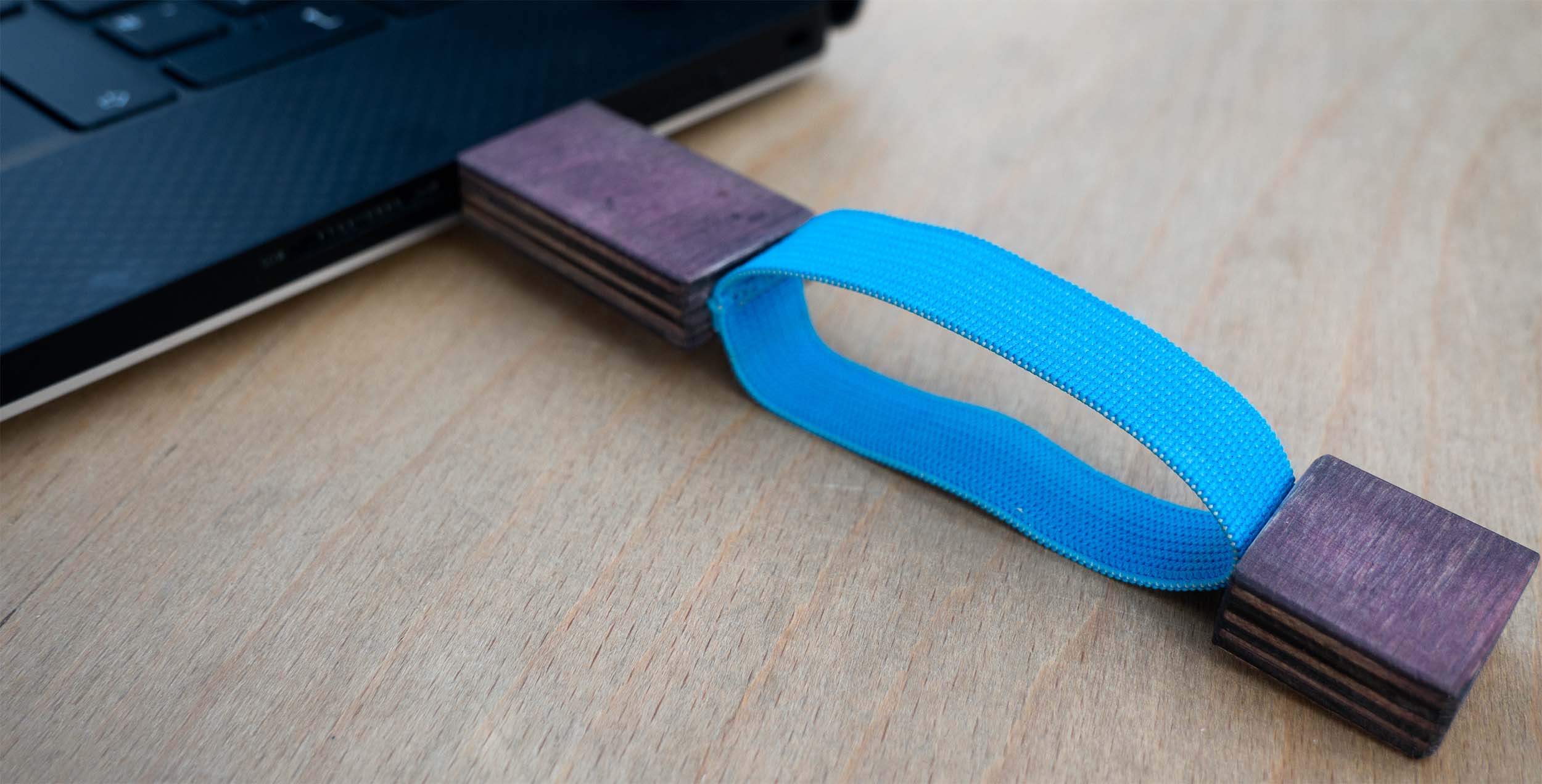 USB-Stick aus dunklem Holz eingesteckt an Laptop. Deckel des USB-Sticks mit blauem Gummiband an Stick befestigt